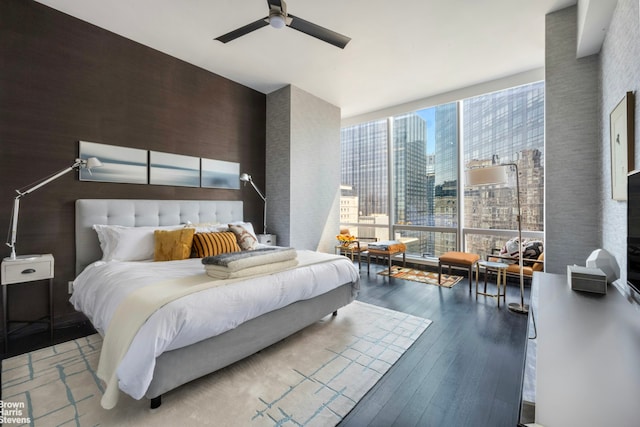 bedroom featuring a view of city, ceiling fan, wood-type flooring, and floor to ceiling windows