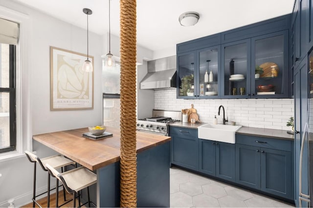 kitchen featuring blue cabinetry, sink, hanging light fixtures, wall chimney range hood, and stove