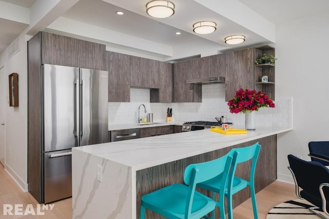 kitchen with sink, a breakfast bar, appliances with stainless steel finishes, light hardwood / wood-style floors, and kitchen peninsula