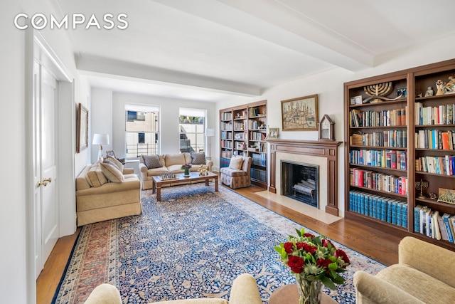 living area featuring a fireplace with flush hearth, beamed ceiling, and wood finished floors