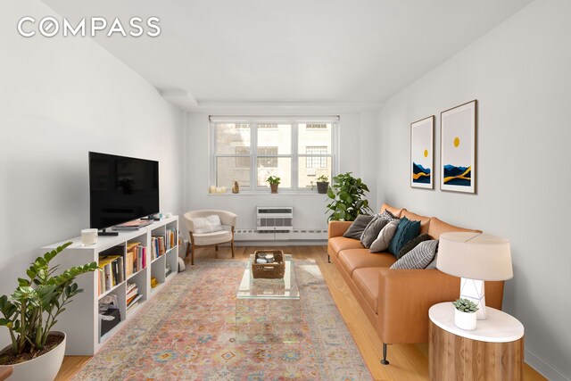 living room featuring an AC wall unit, baseboard heating, and light wood-type flooring