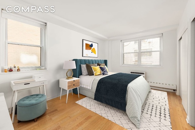 bedroom with a baseboard heating unit and light hardwood / wood-style flooring