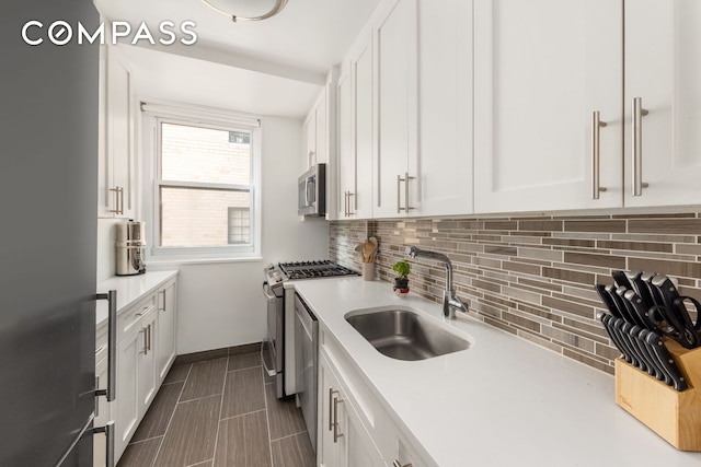 kitchen featuring stainless steel appliances, a sink, white cabinetry, light countertops, and decorative backsplash