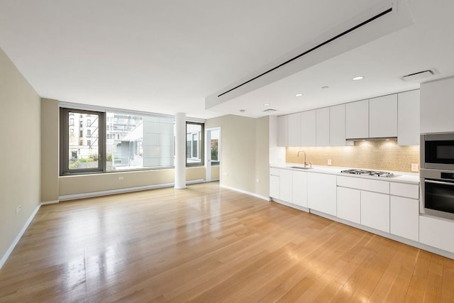 kitchen featuring appliances with stainless steel finishes, light hardwood / wood-style floors, white cabinets, and backsplash