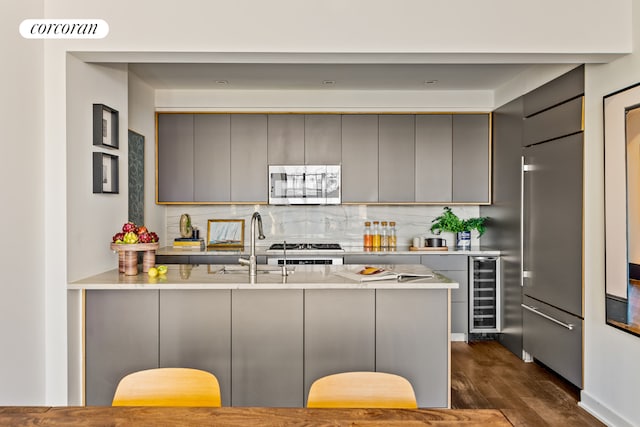 kitchen with beverage cooler, a peninsula, light countertops, appliances with stainless steel finishes, and gray cabinets