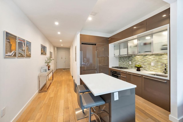 kitchen with light hardwood / wood-style floors, a breakfast bar area, stainless steel appliances, tasteful backsplash, and a center island