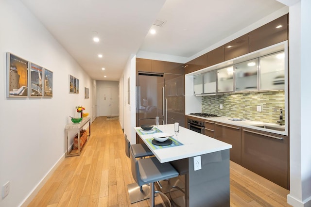 kitchen with backsplash, light hardwood / wood-style floors, a center island, a breakfast bar area, and stainless steel appliances