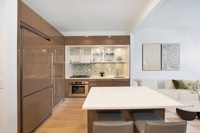 kitchen featuring decorative backsplash, sink, light wood-type flooring, a kitchen breakfast bar, and stainless steel appliances