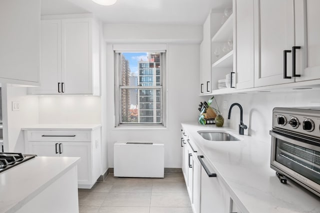 kitchen featuring dishwasher, sink, white cabinetry, light tile patterned floors, and light stone counters