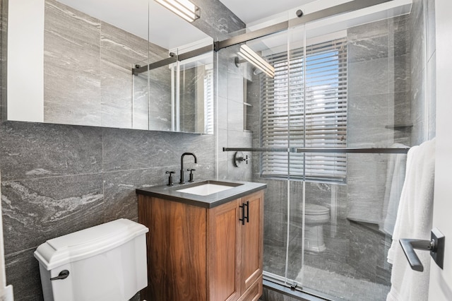 bathroom with toilet, tile walls, a shower with door, and vanity