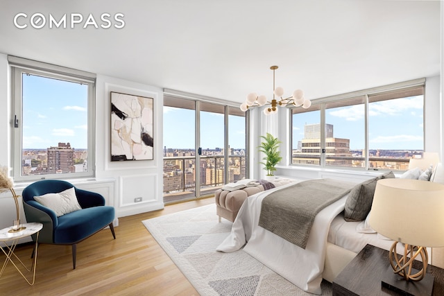 bedroom featuring access to exterior, a city view, a chandelier, and light wood-style floors