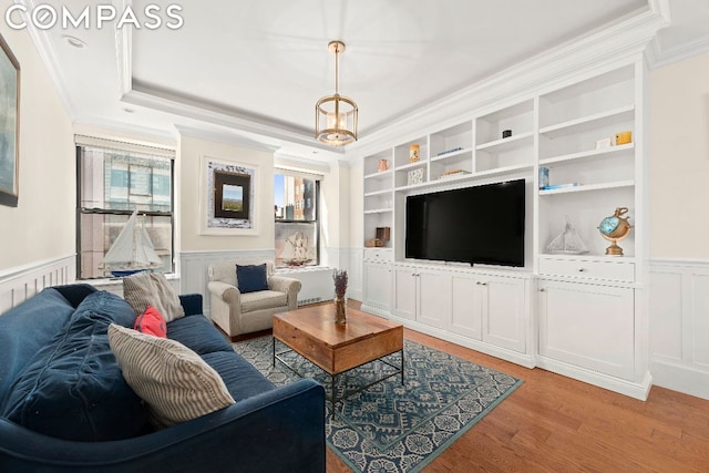 living room with hardwood / wood-style flooring, a raised ceiling, a chandelier, crown molding, and built in shelves