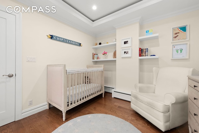 bedroom with a tray ceiling, ornamental molding, wood finished floors, a crib, and baseboards