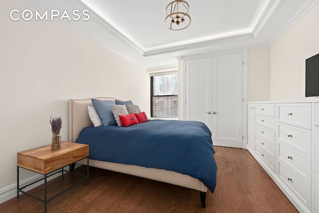 bedroom featuring dark wood-style floors, ornamental molding, a raised ceiling, and a chandelier