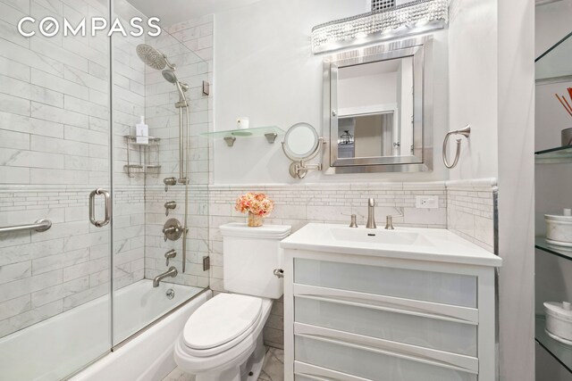 bathroom with wainscoting, toilet, shower / bath combination with glass door, vanity, and tile walls