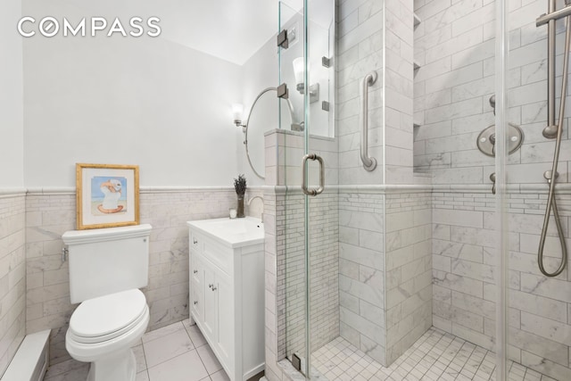 bathroom featuring toilet, a wainscoted wall, vanity, tile walls, and a stall shower