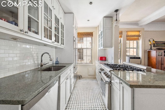 kitchen with white cabinets, appliances with stainless steel finishes, dark stone countertops, sink, and backsplash