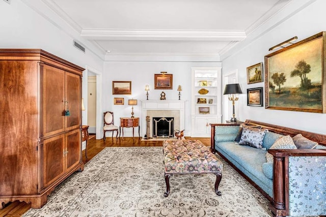 living area featuring visible vents, crown molding, built in features, beamed ceiling, and a fireplace with flush hearth