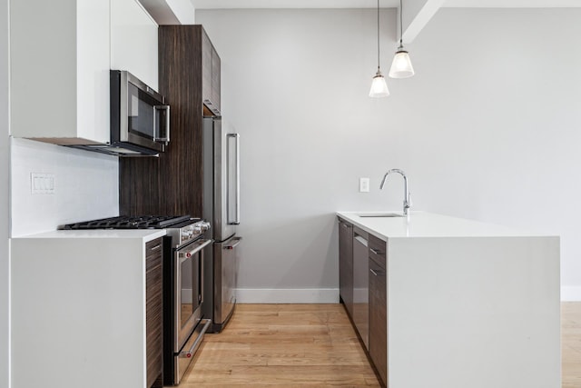 kitchen featuring modern cabinets, appliances with stainless steel finishes, decorative light fixtures, light countertops, and a sink