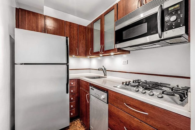 kitchen with stainless steel appliances, a sink, light countertops, and glass insert cabinets