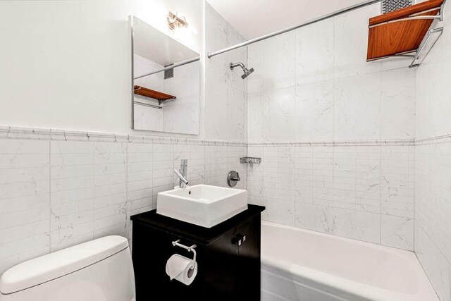 bathroom with tile walls, shower / bath combination, vanity, and toilet