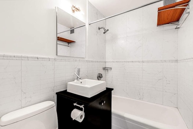 bathroom with tub / shower combination, toilet, vanity, and tile walls