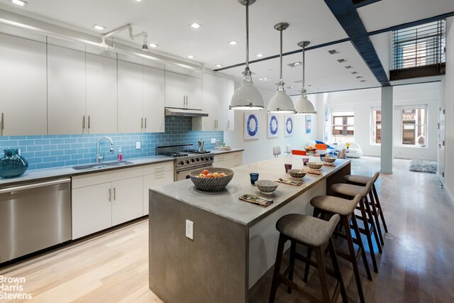 kitchen featuring appliances with stainless steel finishes, a kitchen island, decorative light fixtures, white cabinetry, and sink