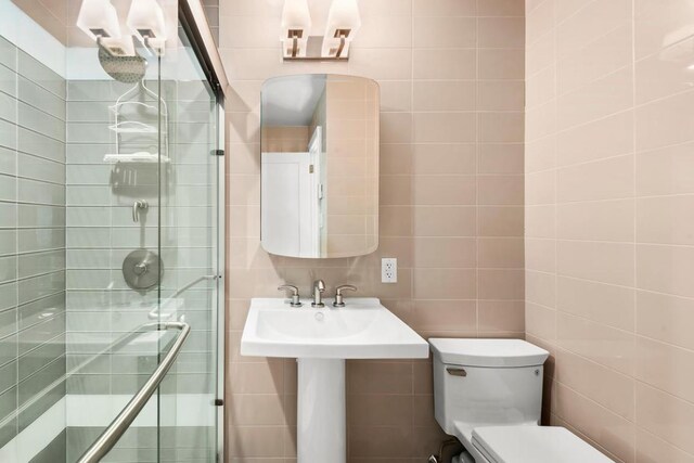 bathroom featuring combined bath / shower with glass door, tile walls, and toilet