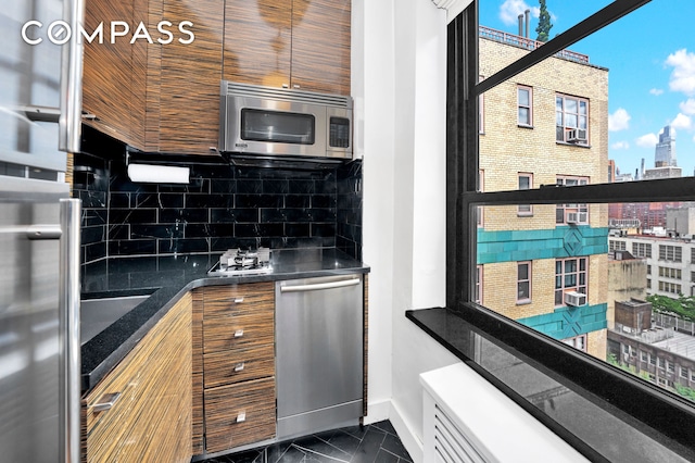 kitchen with baseboards, appliances with stainless steel finishes, dark countertops, marble finish floor, and backsplash