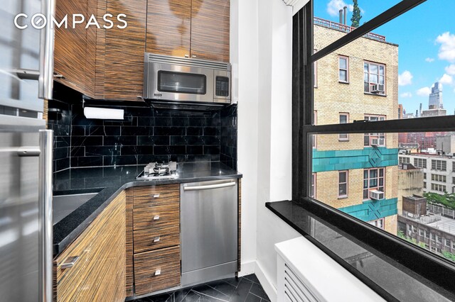 kitchen with stainless steel appliances, baseboards, backsplash, dark countertops, and dark marble finish floors