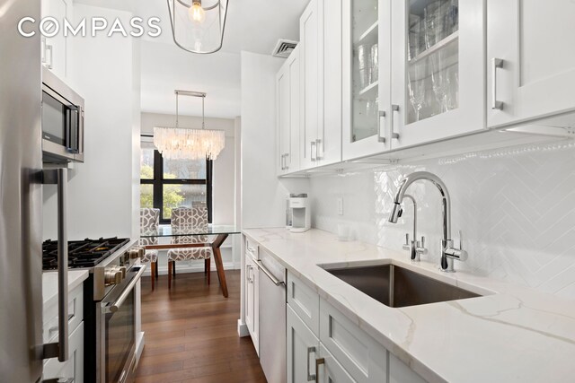 kitchen with appliances with stainless steel finishes, pendant lighting, sink, white cabinets, and light stone countertops