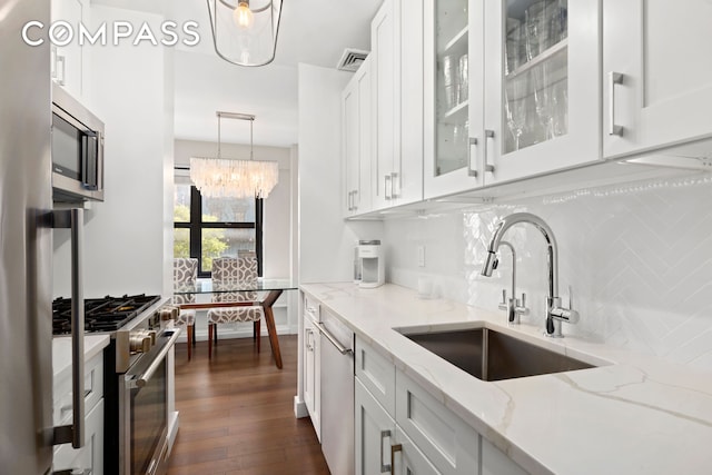 kitchen with an inviting chandelier, white cabinets, a sink, appliances with stainless steel finishes, and backsplash