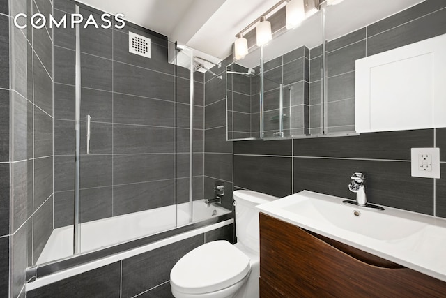 full bathroom with tile walls, tiled shower / bath, vanity, and toilet