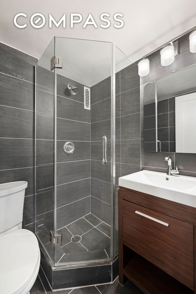 full bath featuring vanity, tile walls, a shower stall, and toilet