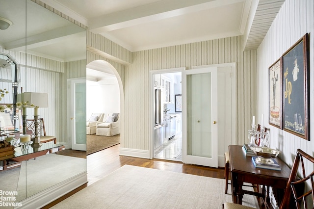 dining room featuring baseboards, arched walkways, wood finished floors, and wallpapered walls