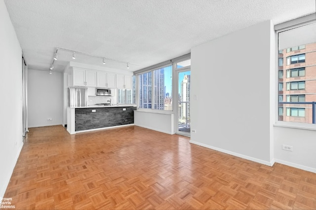 unfurnished living room featuring light parquet flooring, a textured ceiling, and rail lighting