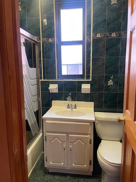 full bathroom with toilet, vanity, shower / bath combination with glass door, and tile walls