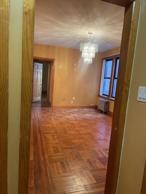 interior space with parquet flooring, radiator, and a notable chandelier