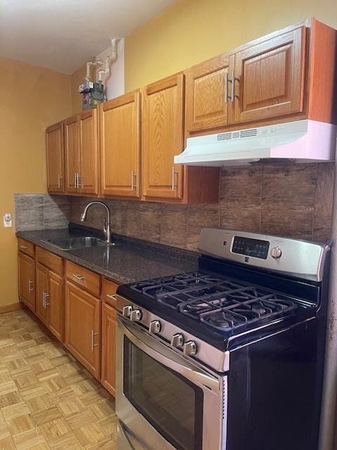 kitchen with tasteful backsplash, sink, gas range, and light parquet floors