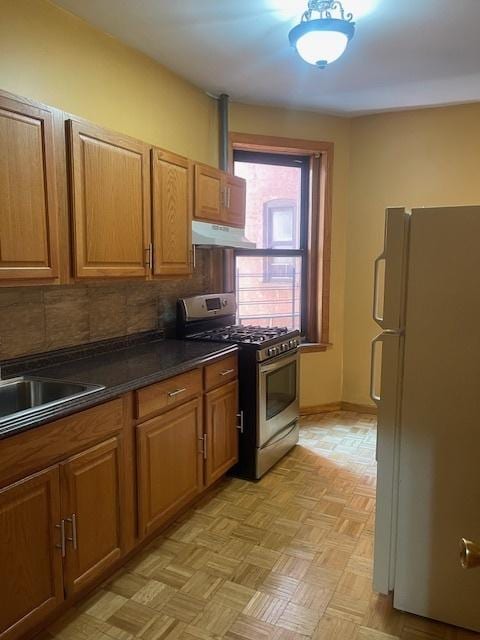 kitchen featuring stainless steel gas stove, tasteful backsplash, sink, light parquet floors, and white fridge