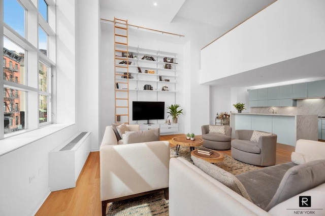 living room featuring built in shelves, a towering ceiling, radiator, and light hardwood / wood-style floors