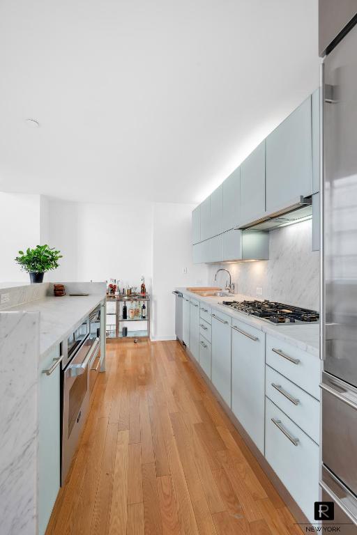 kitchen with sink, stainless steel appliances, light stone counters, light hardwood / wood-style floors, and decorative backsplash