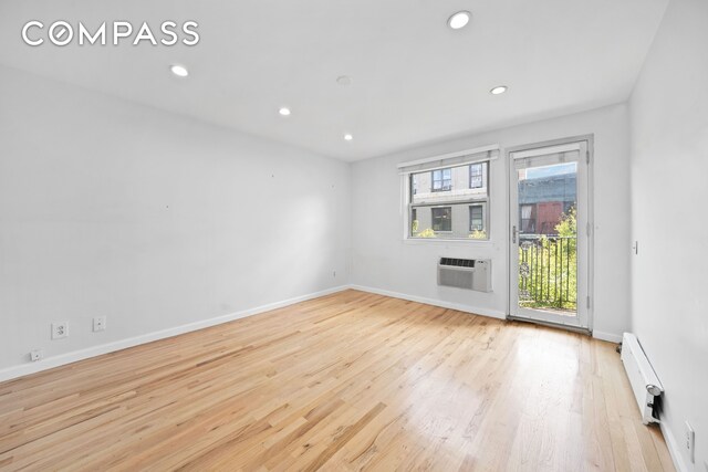 spare room with a baseboard heating unit, wood finished floors, a wall unit AC, recessed lighting, and baseboards