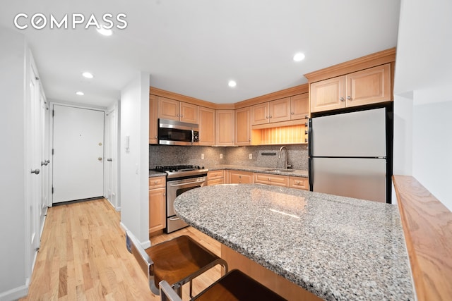 kitchen featuring light stone countertops, a sink, decorative backsplash, stainless steel appliances, and light wood-type flooring