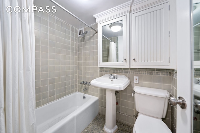 bathroom with tile patterned floors, toilet, a sink, tile walls, and shower / tub combo