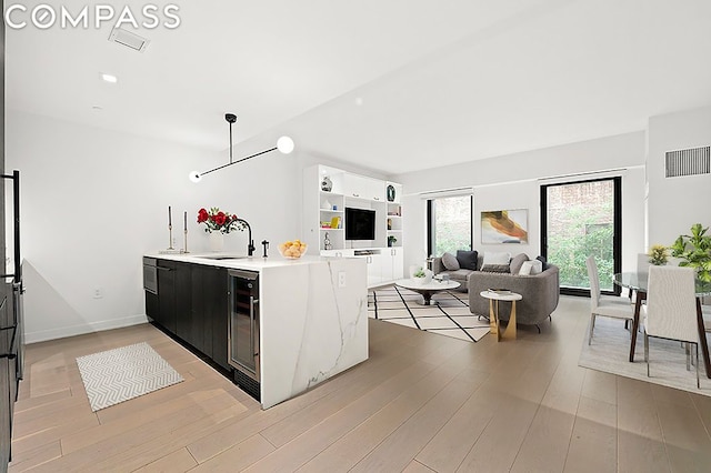 kitchen with light hardwood / wood-style floors, kitchen peninsula, wine cooler, hanging light fixtures, and sink