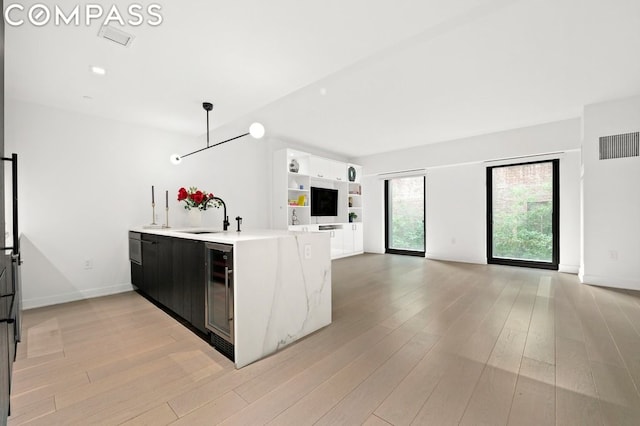 kitchen with kitchen peninsula, light wood-type flooring, wine cooler, hanging light fixtures, and sink