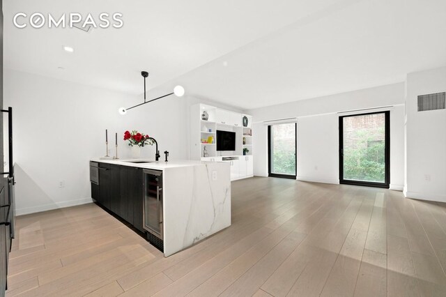 kitchen featuring decorative light fixtures, sink, wine cooler, kitchen peninsula, and light hardwood / wood-style flooring