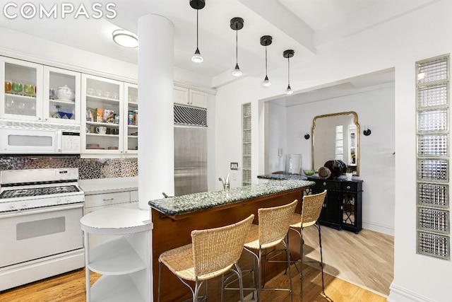 kitchen with white appliances, a kitchen breakfast bar, white cabinets, hanging light fixtures, and light hardwood / wood-style flooring