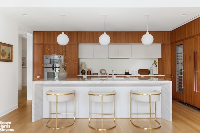 kitchen with modern cabinets, a breakfast bar area, brown cabinetry, and light wood finished floors